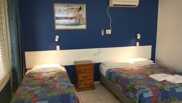 A room with two beds, a small wooden nightstand, a wall-mounted air conditioner, and a painting above the beds.