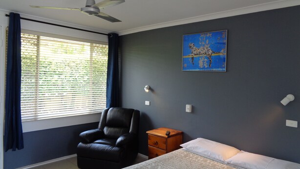 A bedroom with a bed, a chair, a nightstand, a ceiling fan, and a window with blinds. - Aspley Sunset Motel (Aspley)