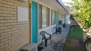 A motel with a brick facade, air conditioning units, outdoor seating, and a small garden area. - Aspley Sunset Motel (Aspley)