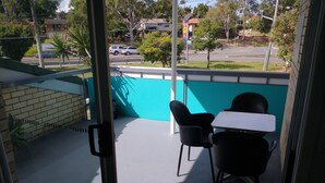 A balcony with two black chairs and a small table, overlooking a street with cars and buildings. - Aspley Sunset Motel (Aspley)