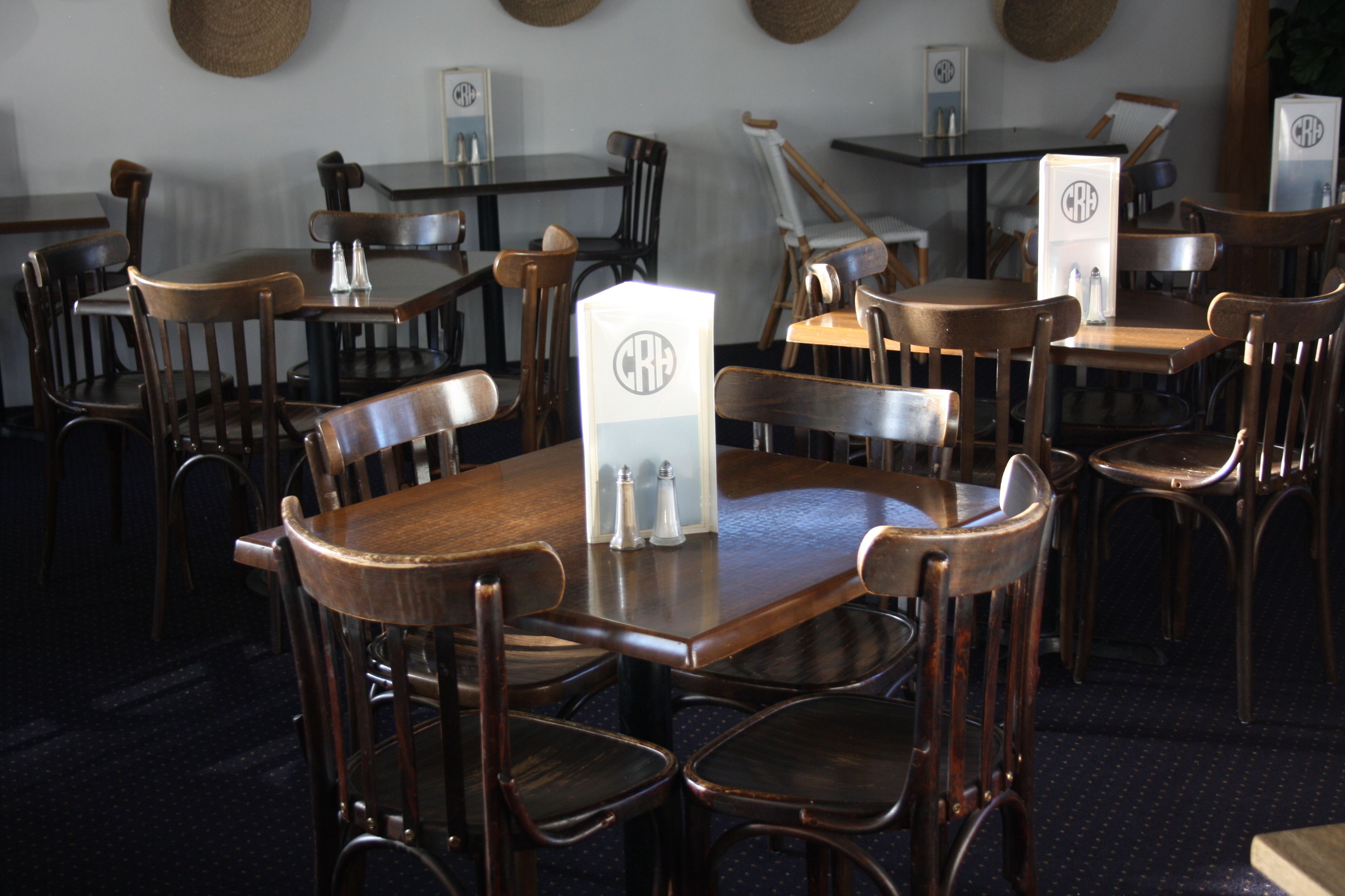 Een restaurant met houten tafels en stoelen, zout- en pepervaatjes en een menukaart met een logo.
