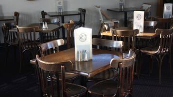 Een restaurant met houten tafels en stoelen, zout- en pepervaatjes en een menukaart met een logo.