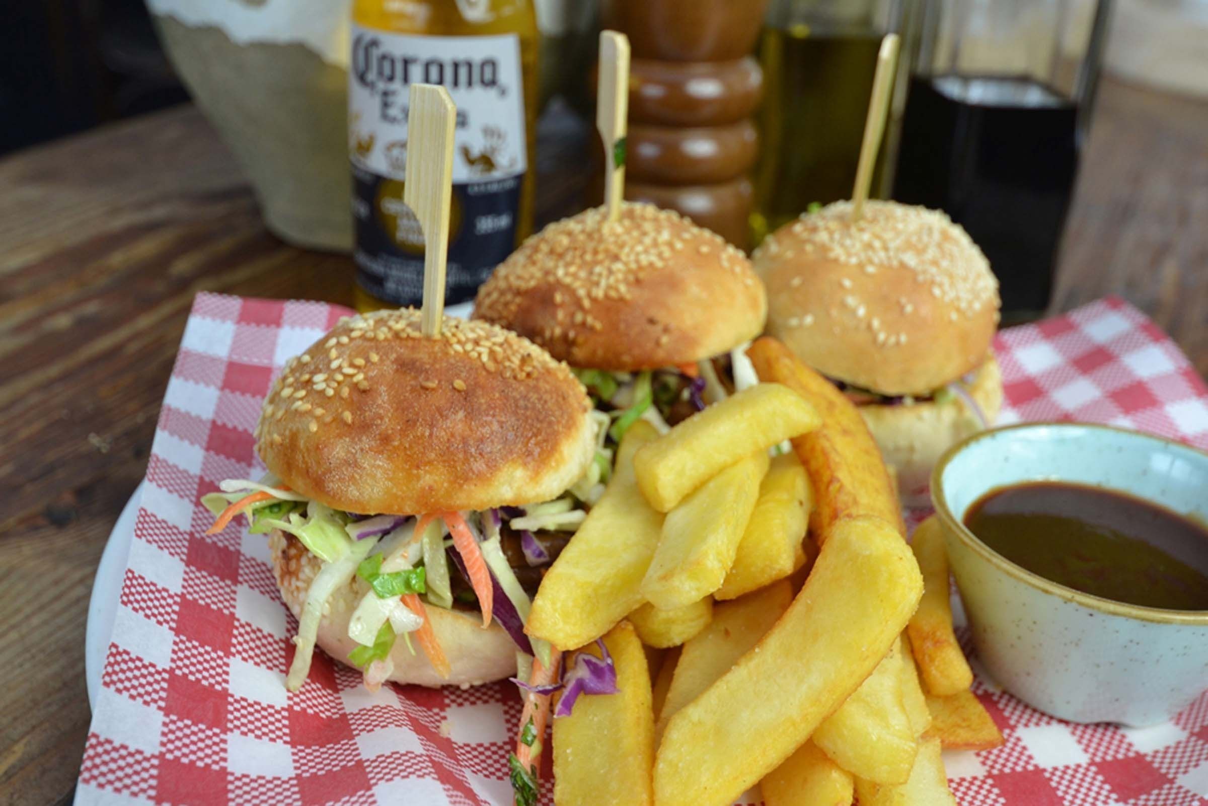 Comida que incluye dos hamburguesas sujetas con palillos, una porción de papas fritas y un tazón pequeño de salsa sobre un mantel a cuadros.