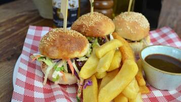 Comida que incluye dos hamburguesas sujetas con palillos, una porción de papas fritas y un tazón pequeño de salsa sobre un mantel a cuadros.