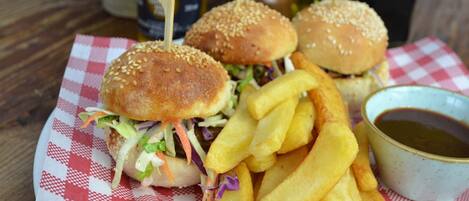 Comida que incluye dos hamburguesas sujetas con palillos, una porción de papas fritas y un tazón pequeño de salsa sobre un mantel a cuadros.