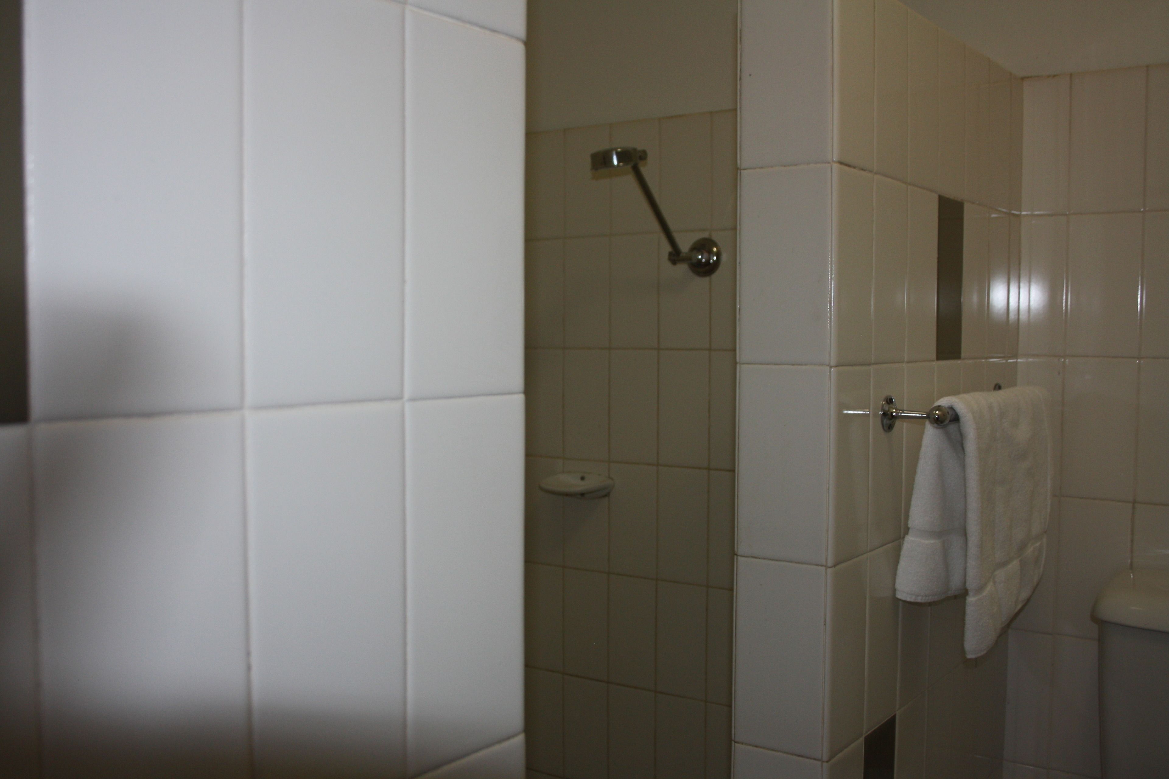 Une salle de bain carrelée de blanc, une douche avec un pommeau de douche amovible et une serviette suspendue à un porte-serviettes.