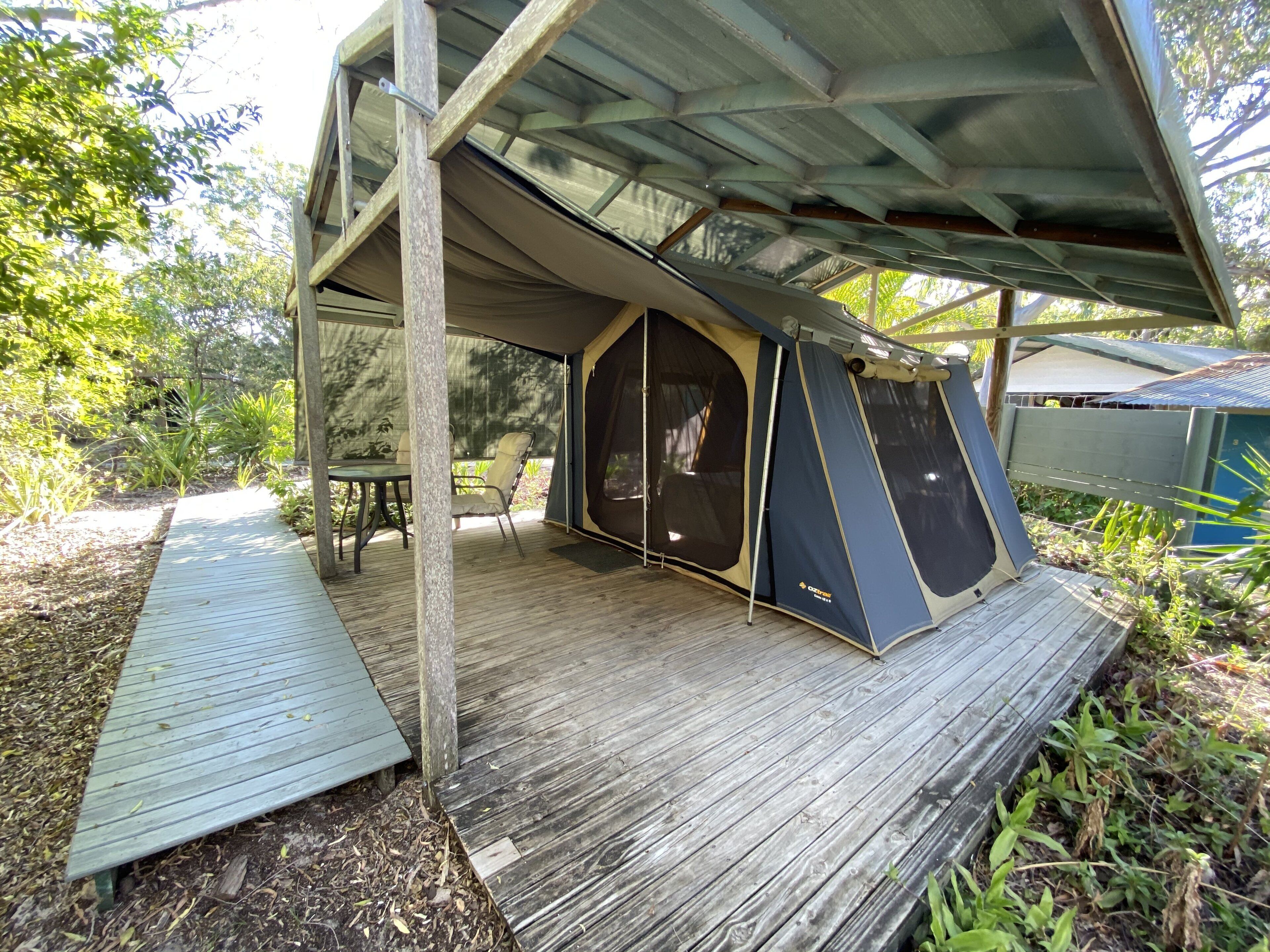 Een kampeerterrein met een tent, een houten terras en een tafel met stoelen.