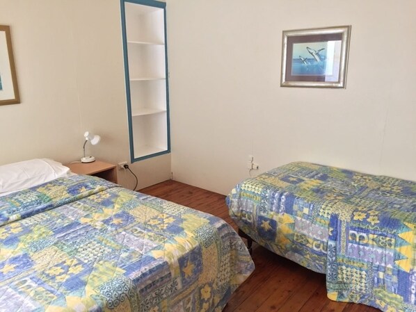 A bedroom with two beds, a nightstand, a wall-mounted shelf, and a framed picture.