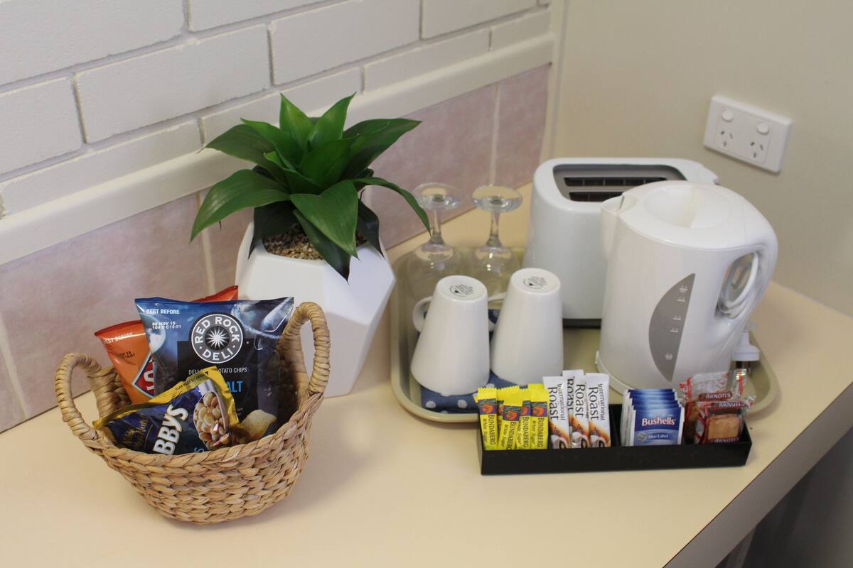 En köksbänk med en kaffebryggare, en brödrost och en korg som innehåller snacks och en växt.