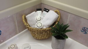 A bathroom with a wicker basket containing toiletries, a potted plant, and a white bathtub. - Motel Northview Mackay (Mount Pleasant)