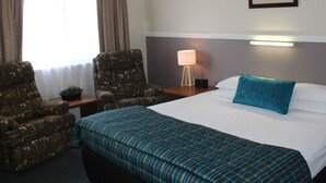 A hotel room with a large bed, two armchairs, a bedside table with a lamp, and a framed picture on the wall. - Motel Northview Mackay (Mount Pleasant)
