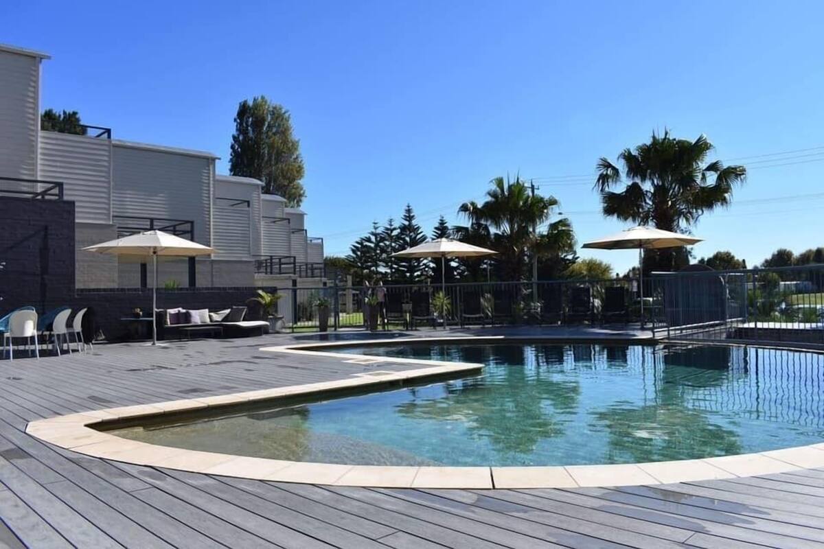 A swimming pool with a wooden deck, lounge chairs, and umbrellas.