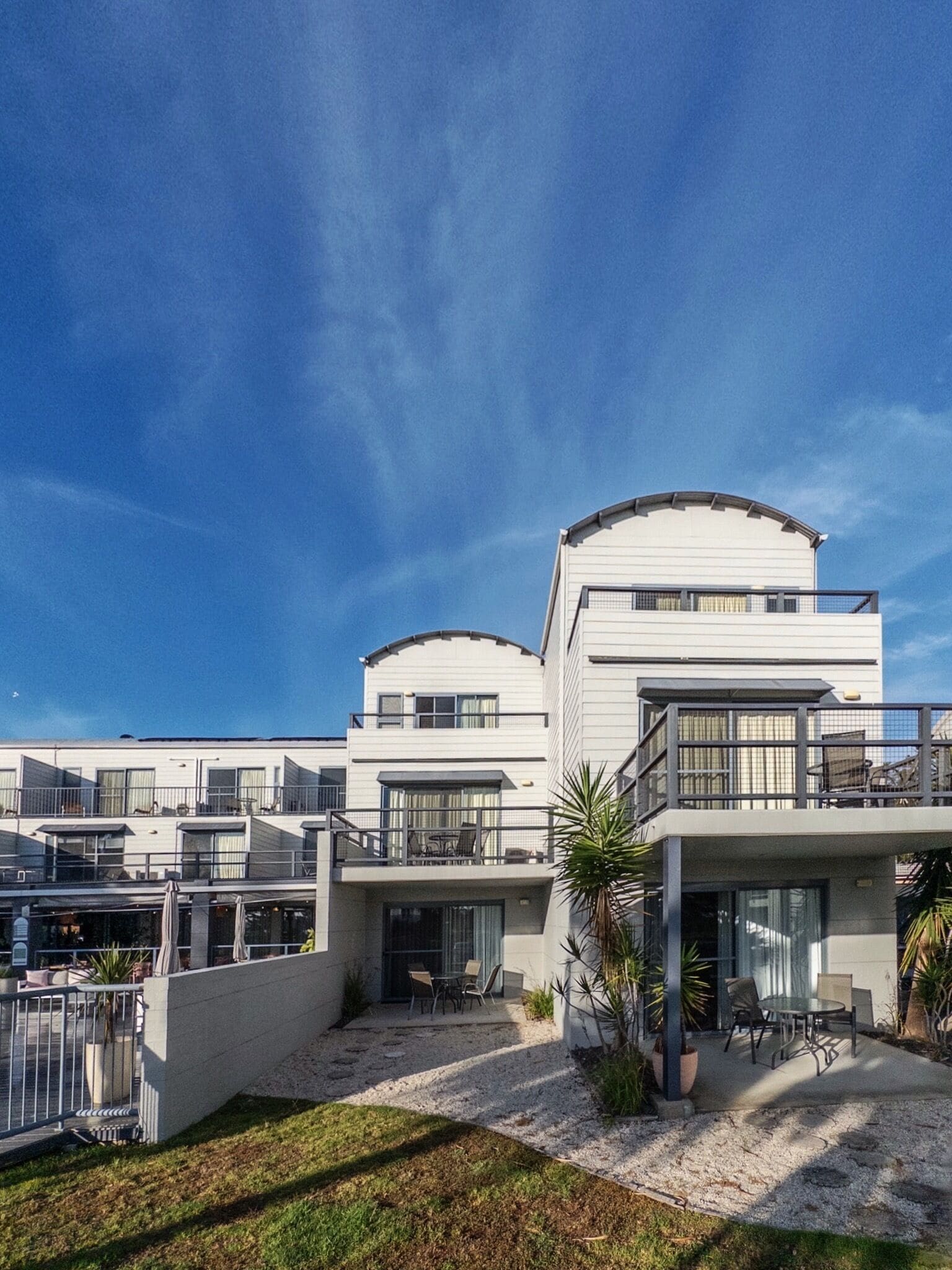 A modern multi-story building with balconies, outdoor seating, and a clear sky.