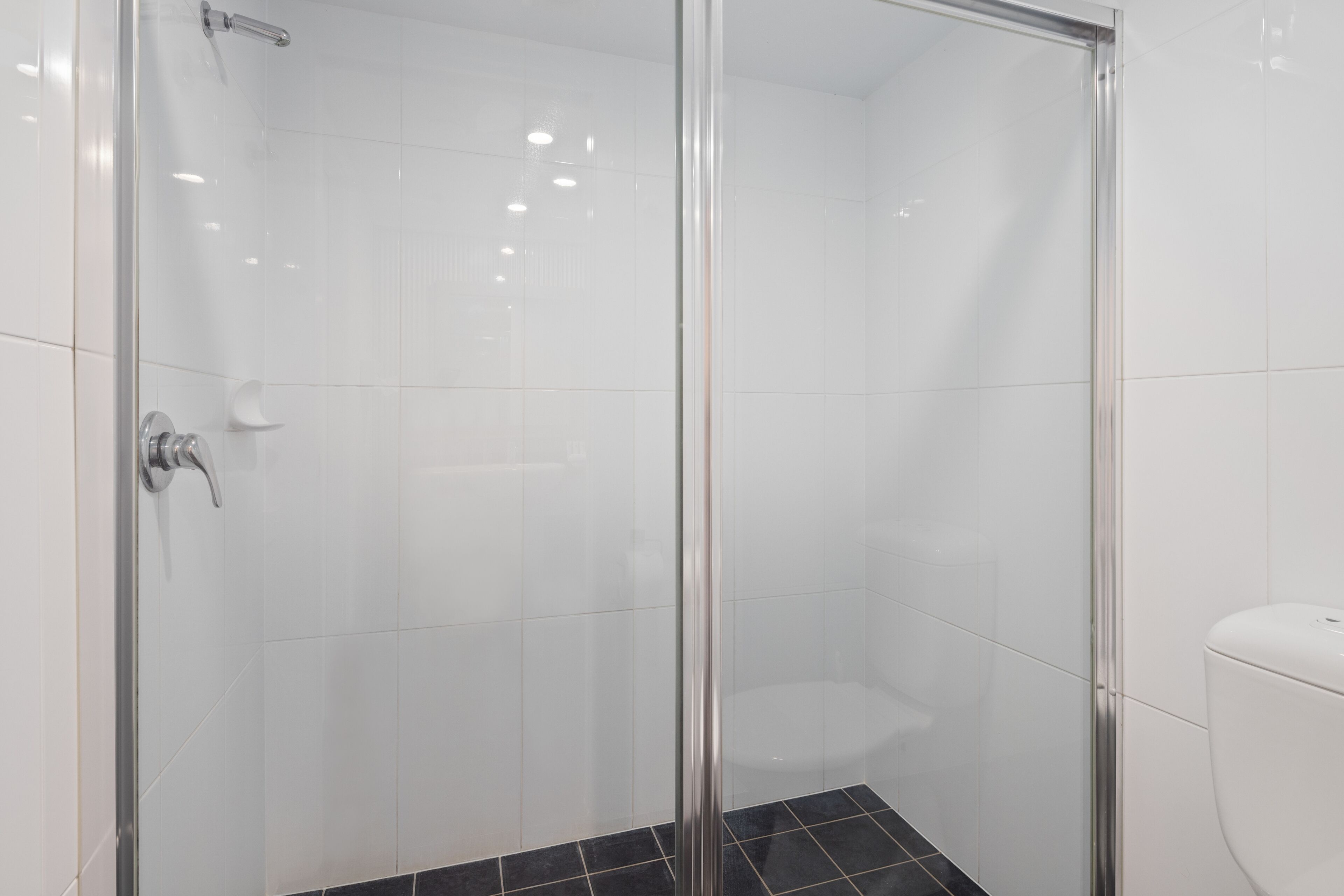 Un baño moderno con cabina de ducha de vidrio, azulejos blancos y suelo de baldosas negras.