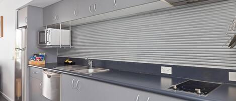 A modern kitchen with grey cabinets, a stainless steel refrigerator, a microwave, a sink, and a built-in stove.