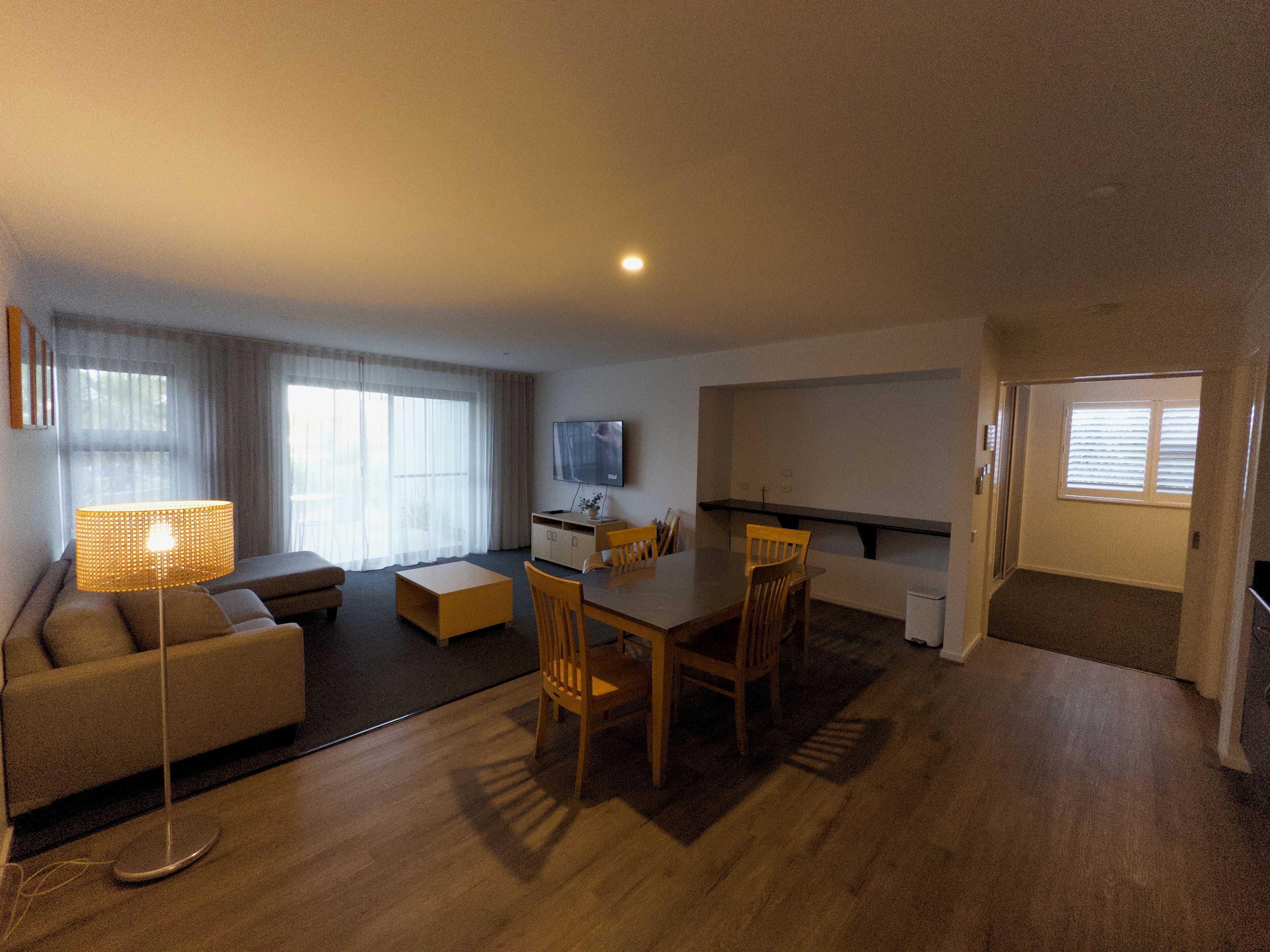 A modern living room with a sofa, a coffee table, a dining table with chairs, a TV, and a lamp.