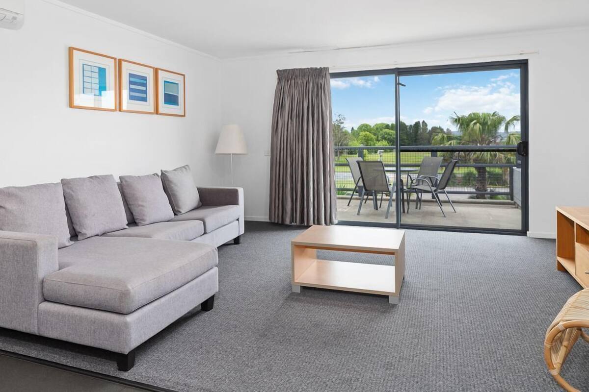A modern living room with a grey sofa, a wooden coffee table, and a balcony with outdoor furniture.