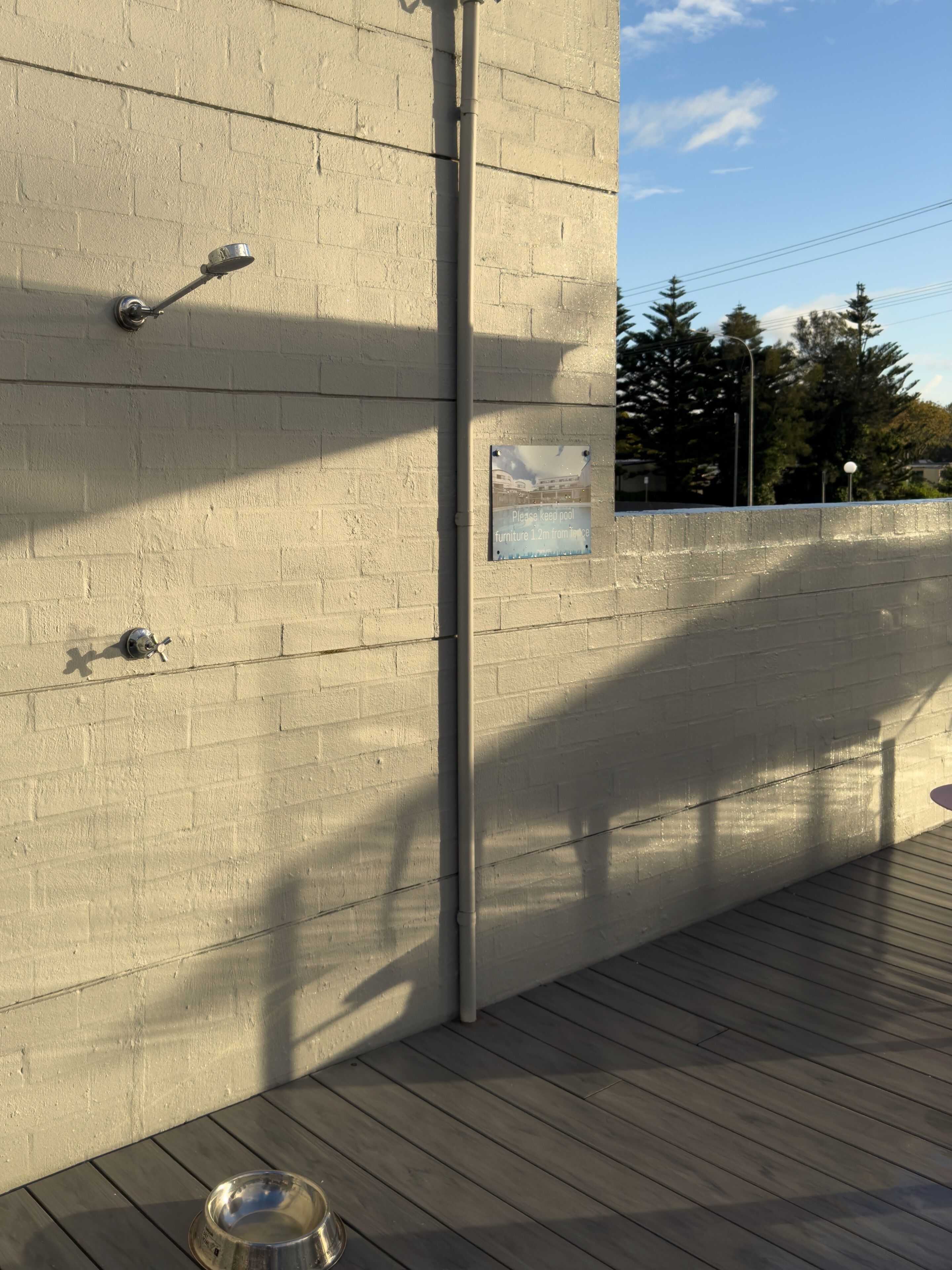 A concrete wall with a metal pipe, a metal bowl, and a sign instructing to keep pool furniture 1.2m from the wall.