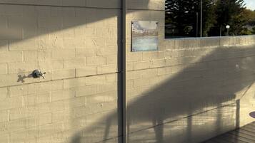 A concrete wall with a metal pipe, a metal bowl, and a sign instructing to keep pool furniture 1.2m from the wall.