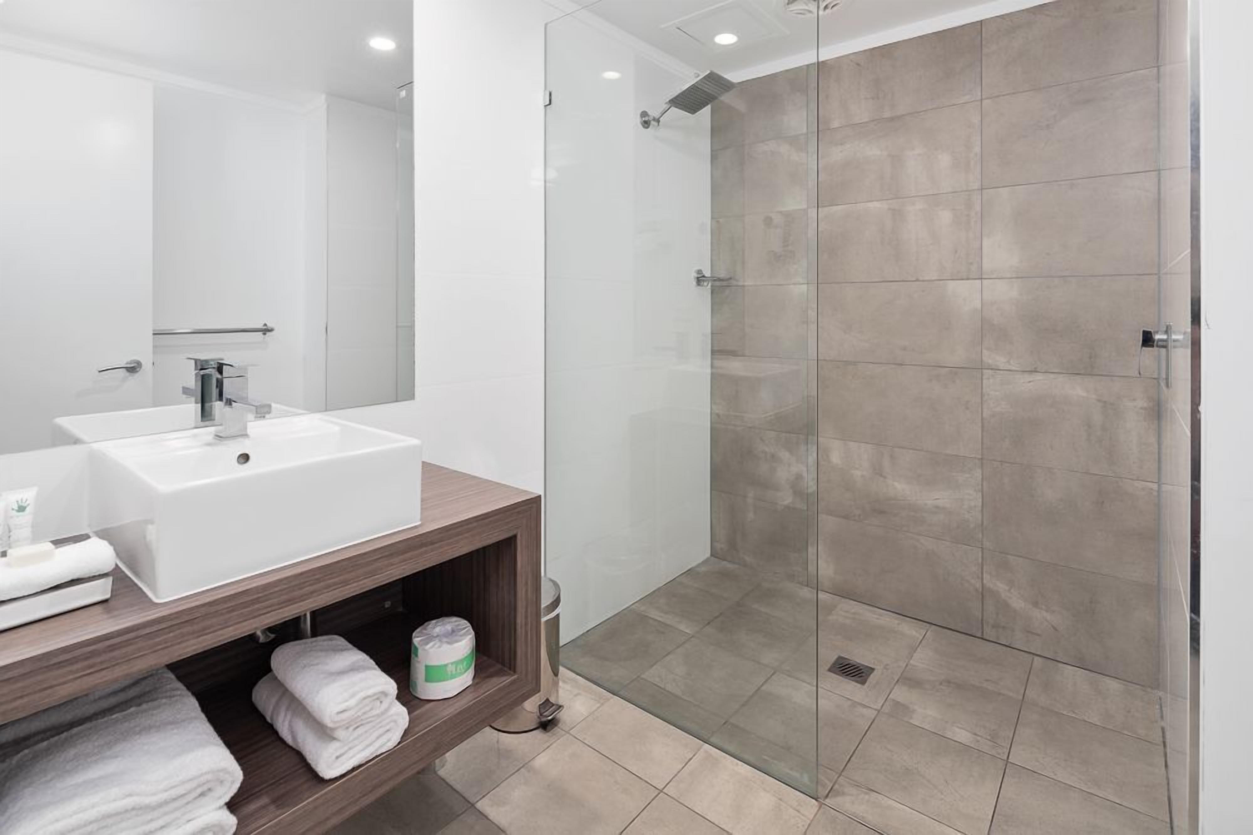 A modern bathroom with a white sink, mirror, and glass shower enclosure.
