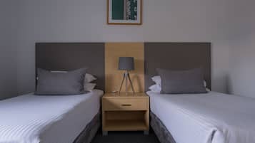 Une chambre d’hôtel avec deux lits simples, une table de chevet en bois avec une lampe et un tableau encadré au mur.