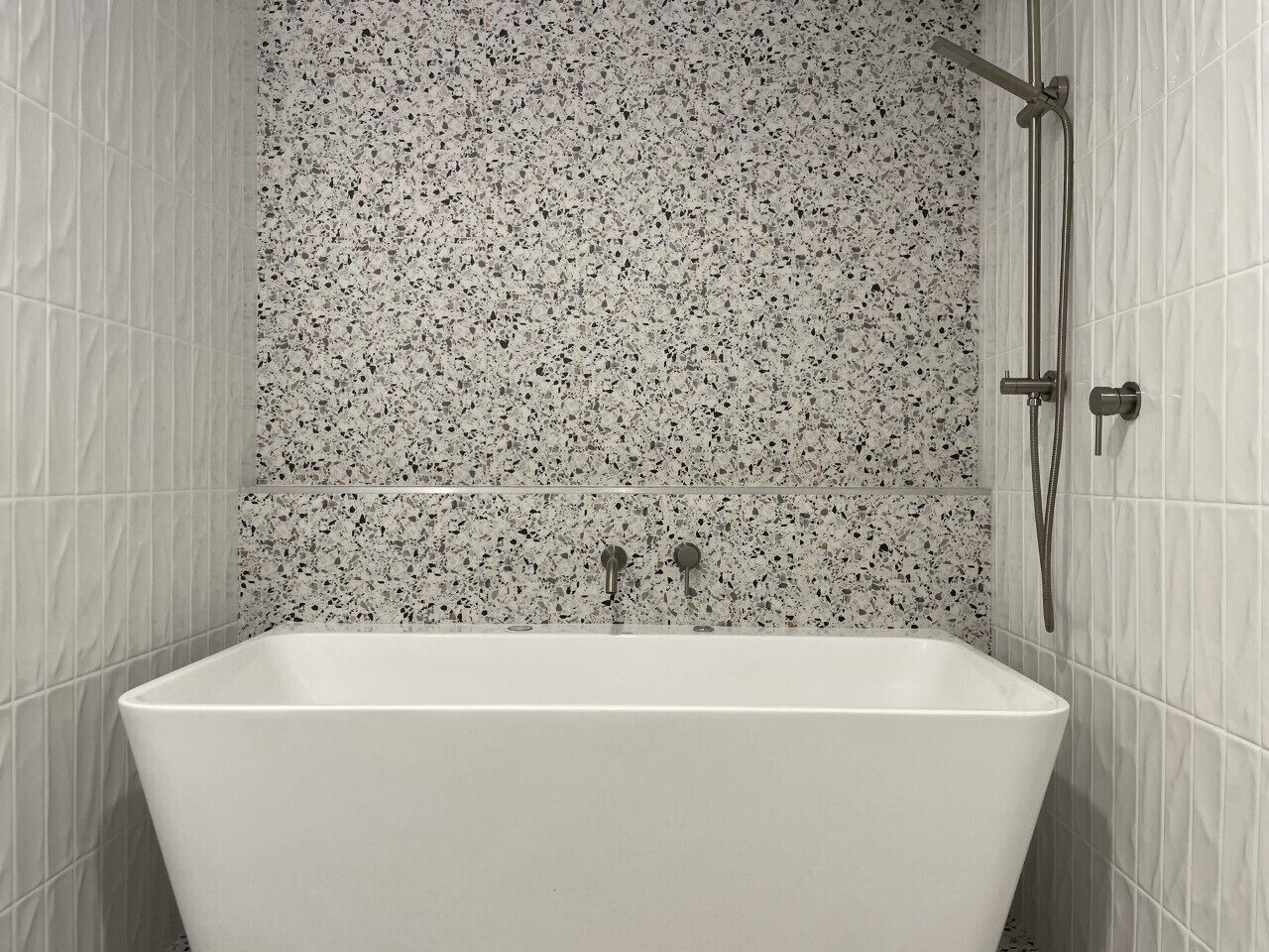 A modern bathroom with a freestanding bathtub, a shower area, and speckled tile walls.