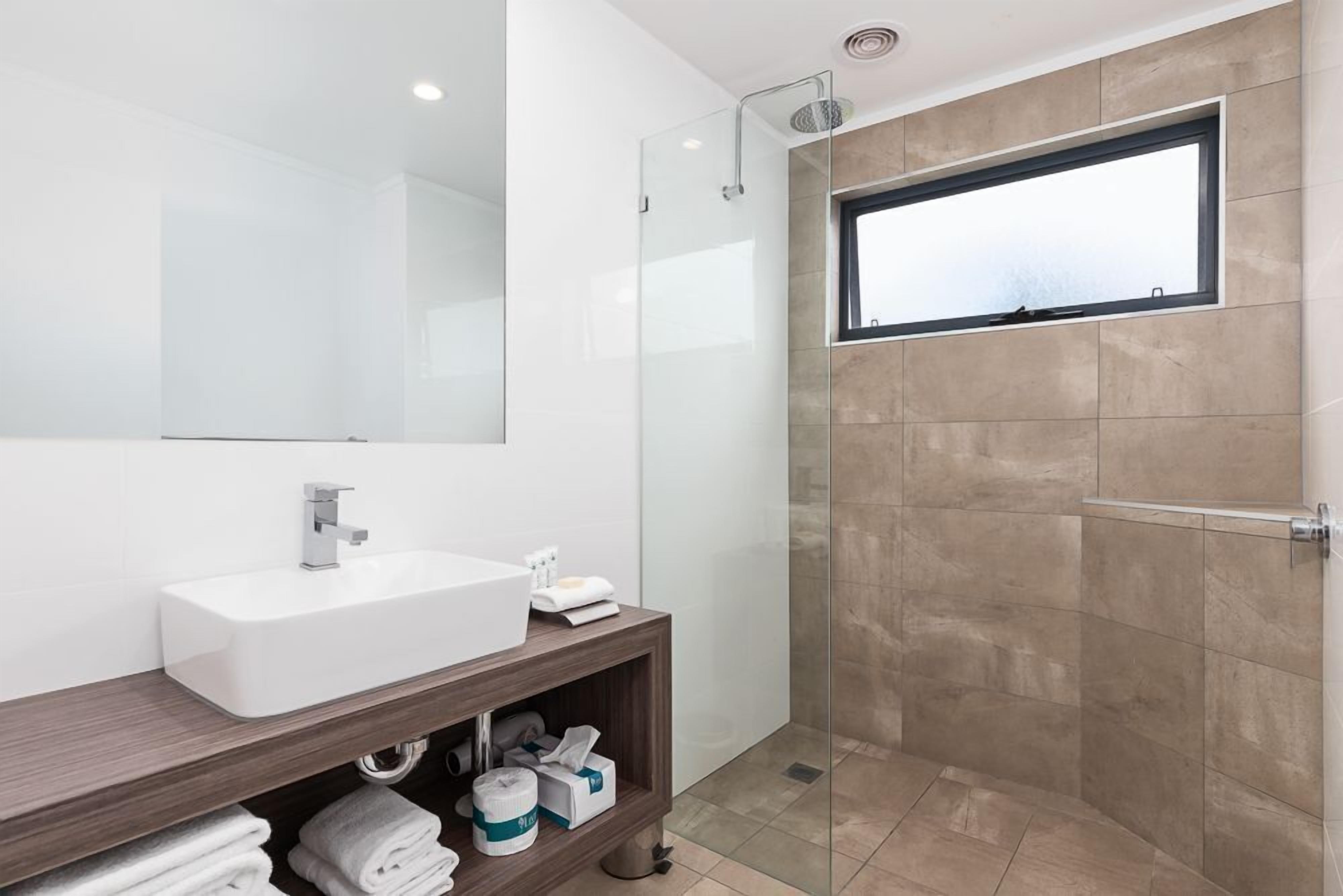 A modern bathroom with a white sink, a glass shower enclosure, and a window above the shower.
