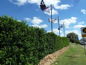 A well-maintained hedge, a stone wall, and a clear blue sky with clouds. - Mandalay Motel (Roma)