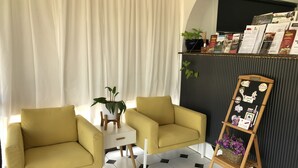 Une pièce avec deux fauteuils jaunes, une petite table blanche, une plante en pot et un présentoir à menu en forme de tableau noir.