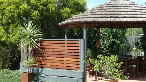 Un banc en bois, un kiosque à toit de chaume et une plante en pot, le tout dans un cadre de jardin.