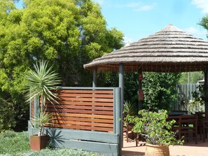 A wooden bench, a thatched-roof gazebo, and a potted plant in a garden setting. - Mandalay Motel (Roma)