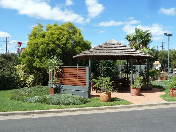 A gazebo with a thatched roof, surrounded by potted plants and a wooden fence. - Mandalay Motel (Roma)
