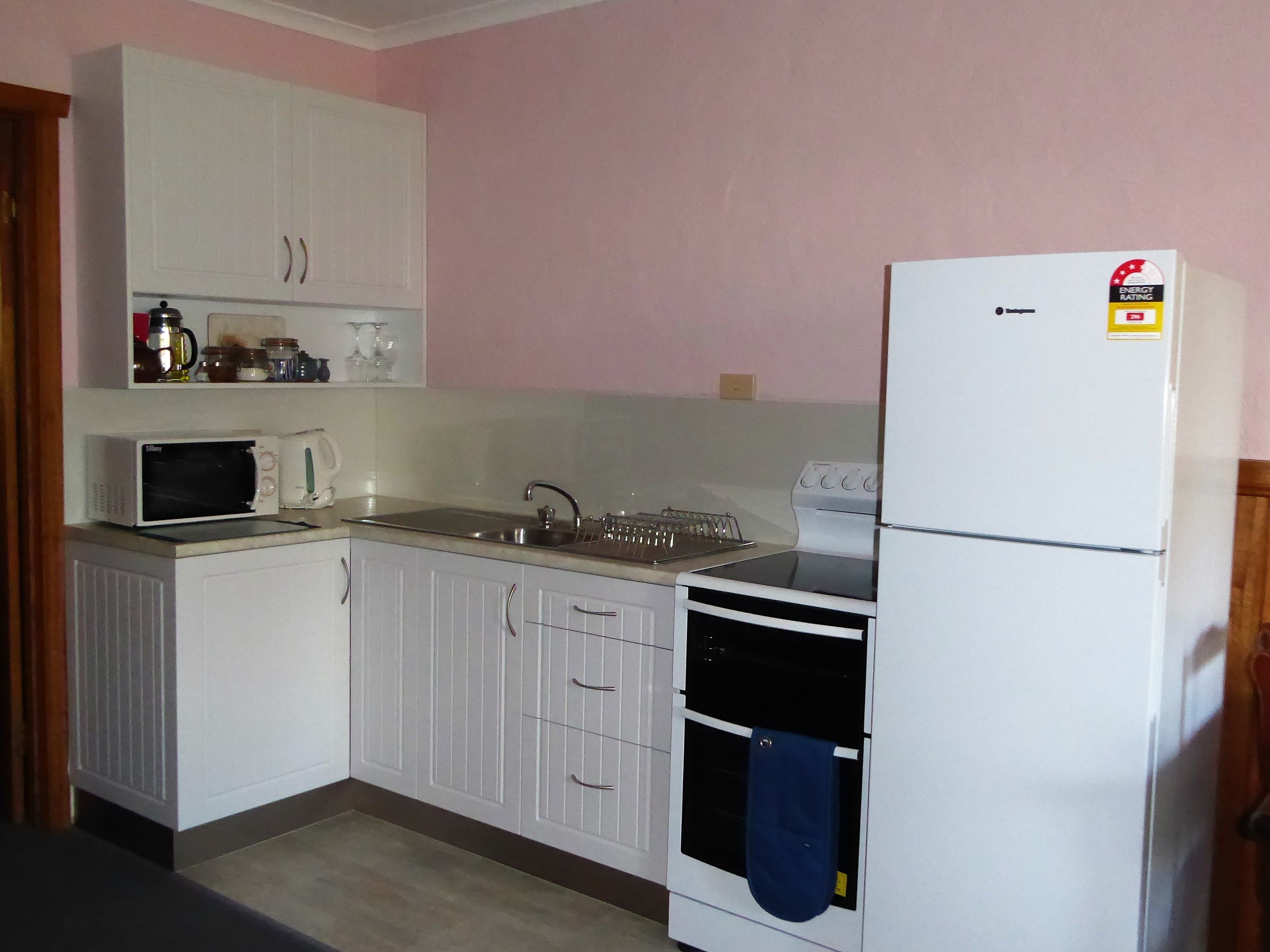Een kleine keuken met witte kasten, een magnetron, een spoelbak, een kookplaat en een koelkast.