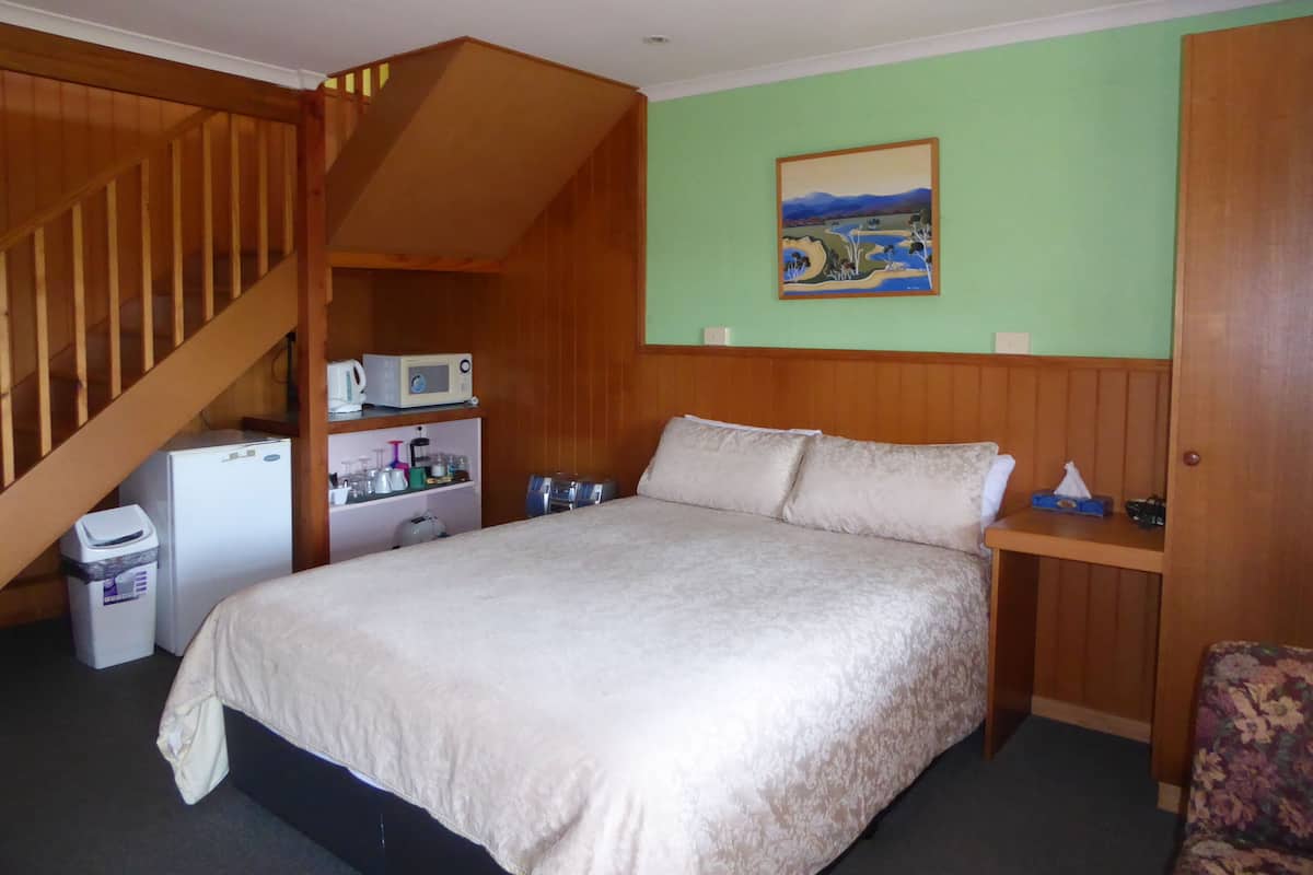 Ein Schlafzimmer mit einem Bett, einer Holztreppe, einer Mikrowelle, einem kleinen Kühlschrank, einem Regal mit verschiedenen Gegenständen und einem Bild an der Wand.