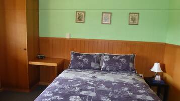 A bedroom with a bed, a wooden nightstand, a lamp, and a wall-mounted shelf.