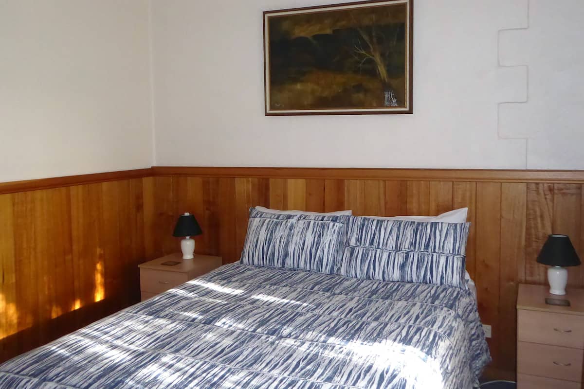 Ein Schlafzimmer mit einem hölzernen Kopfteil, einem Bett mit gestreifter Bettwäsche, zwei Nachttischen mit Lampen und einem Bild an der Wand.