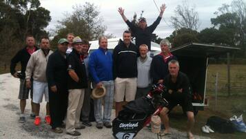 A group of people posing in front of a golf bag and a small shelter.