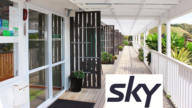A covered outdoor area with a wooden deck, glass doors, and a white railing. - Te Awa Motel (Whanganui)