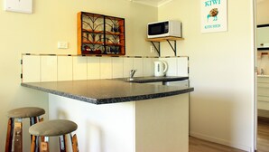 A compact kitchen with a granite countertop, a built-in microwave, a kettle, and a decorative shelf with glassware. - Te Awa Motel (Whanganui)