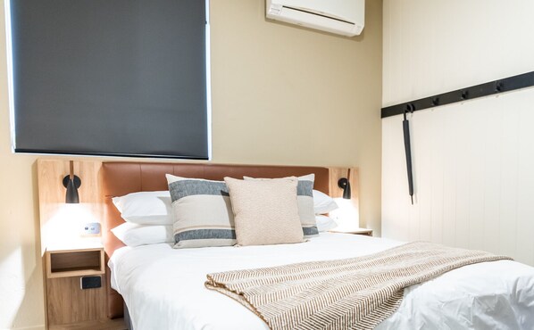Quarto de hotel com uma cama, mesa de cabeceira, luminária e ar condicionado.