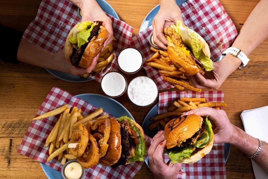 Una mesa con cuatro hamburguesas y papas fritas, cada una acompañada de salsa para mojar.