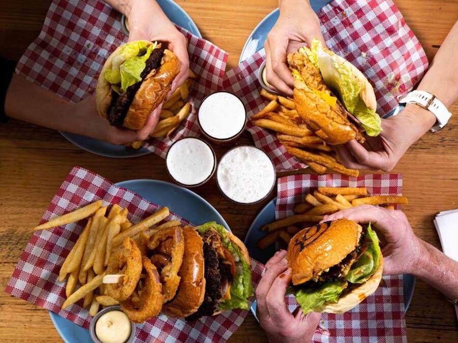 Una mesa con cuatro hamburguesas y papas fritas, cada una acompañada de salsa para mojar.
