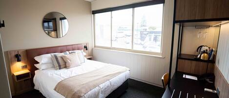 Une chambre d’hôtel avec un grand lit, une table de chevet avec une lampe, un miroir rond, une fenêtre donnant sur l’extérieur et un bureau avec une chaise.
