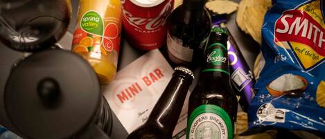 Una varietà di cibi e bevande, tra cui una lattina di Coca-Cola, una bottiglia di Coors Brewery Original Pale Ale, una bottiglia di Whyam Summer Ale, una busta di patatine Smith e un menu del minibar.