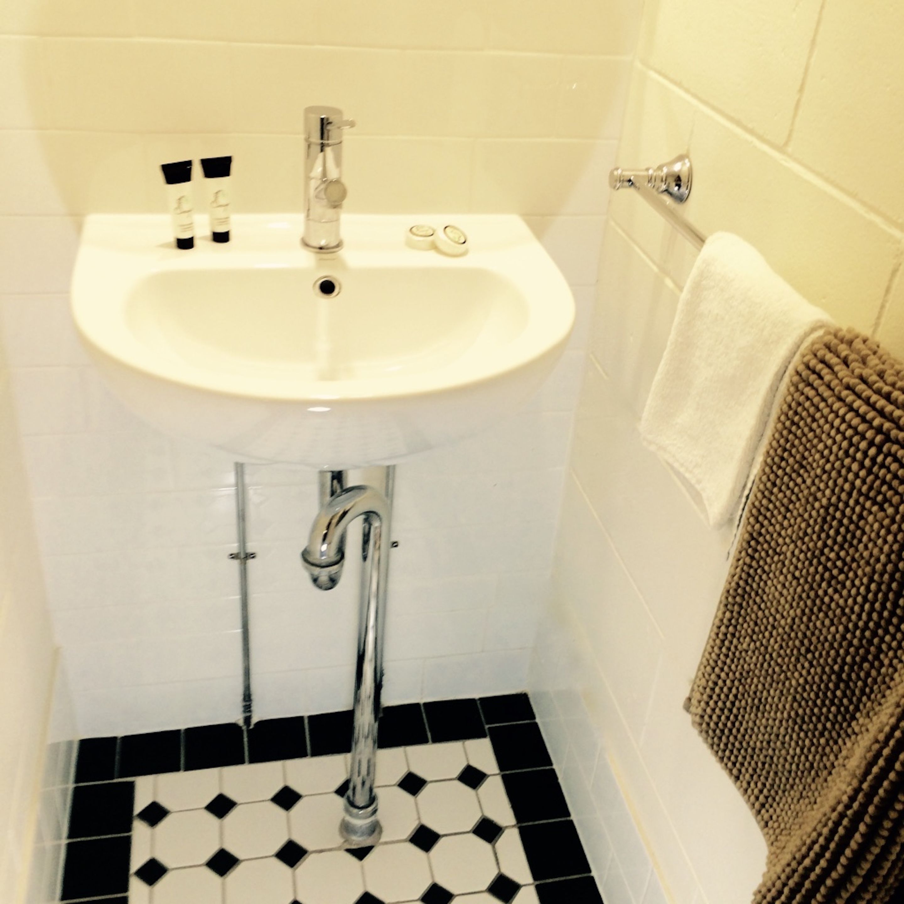 Une salle de bain avec un lavabo blanc, un carrelage noir et blanc au sol et un porte-serviettes sur lequel est posée une serviette marron.