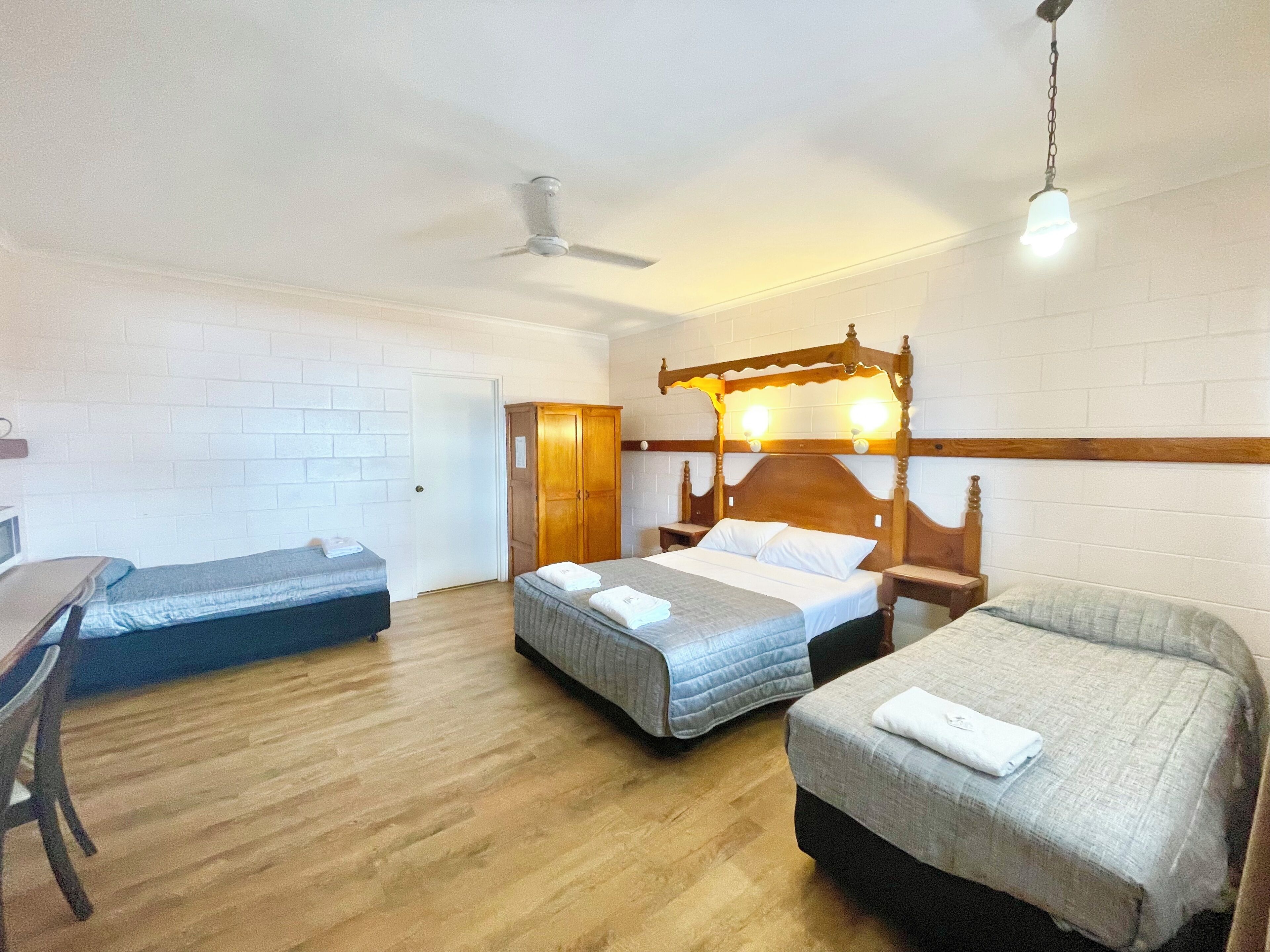 A room with three beds, a wooden wardrobe, a ceiling fan, and a desk with a chair.