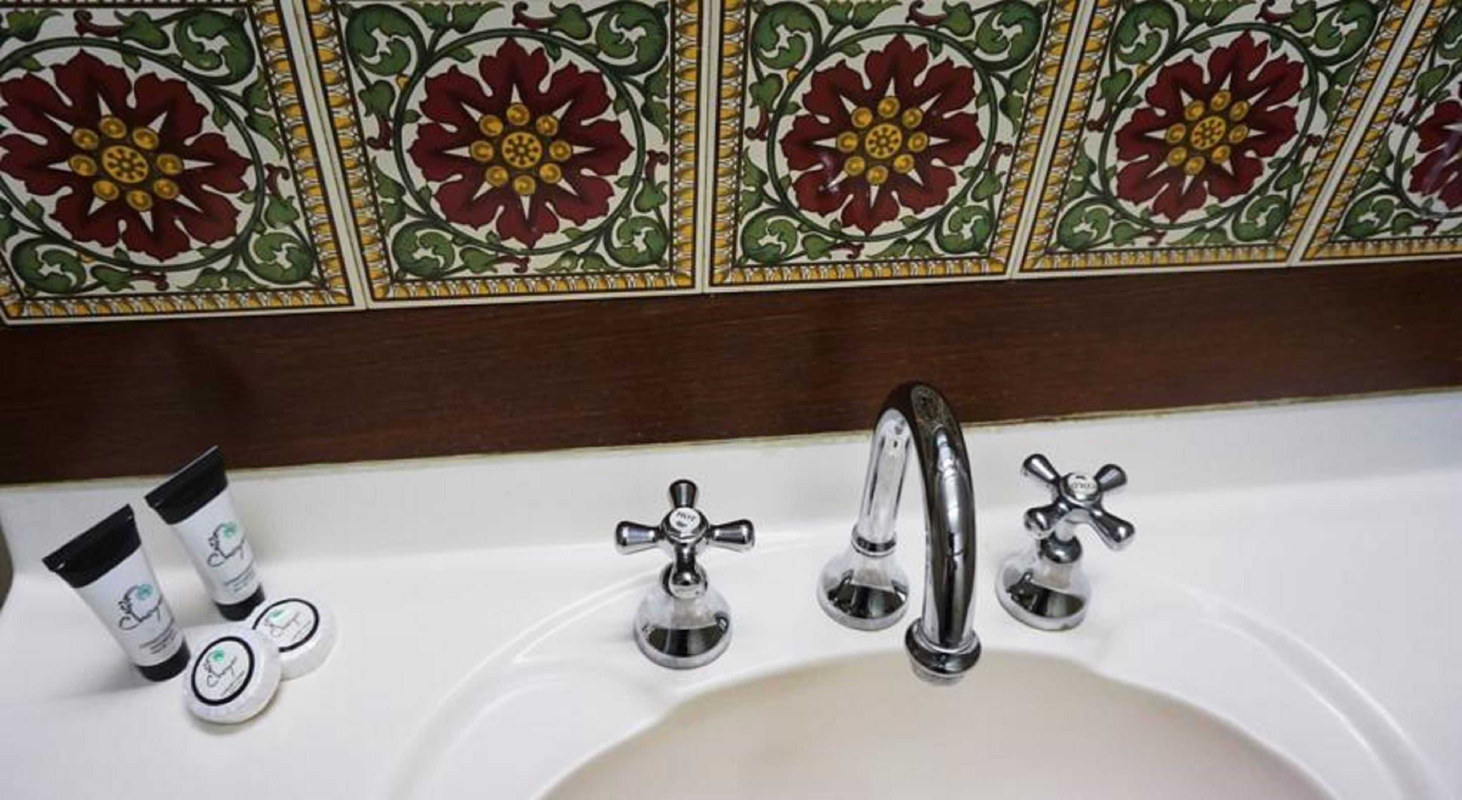 A bathroom with a white sink, three chrome faucets, and decorative tiles with floral patterns.