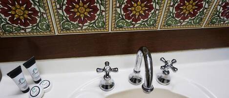 A bathroom with a white sink, three chrome faucets, and decorative tiles with floral patterns.
