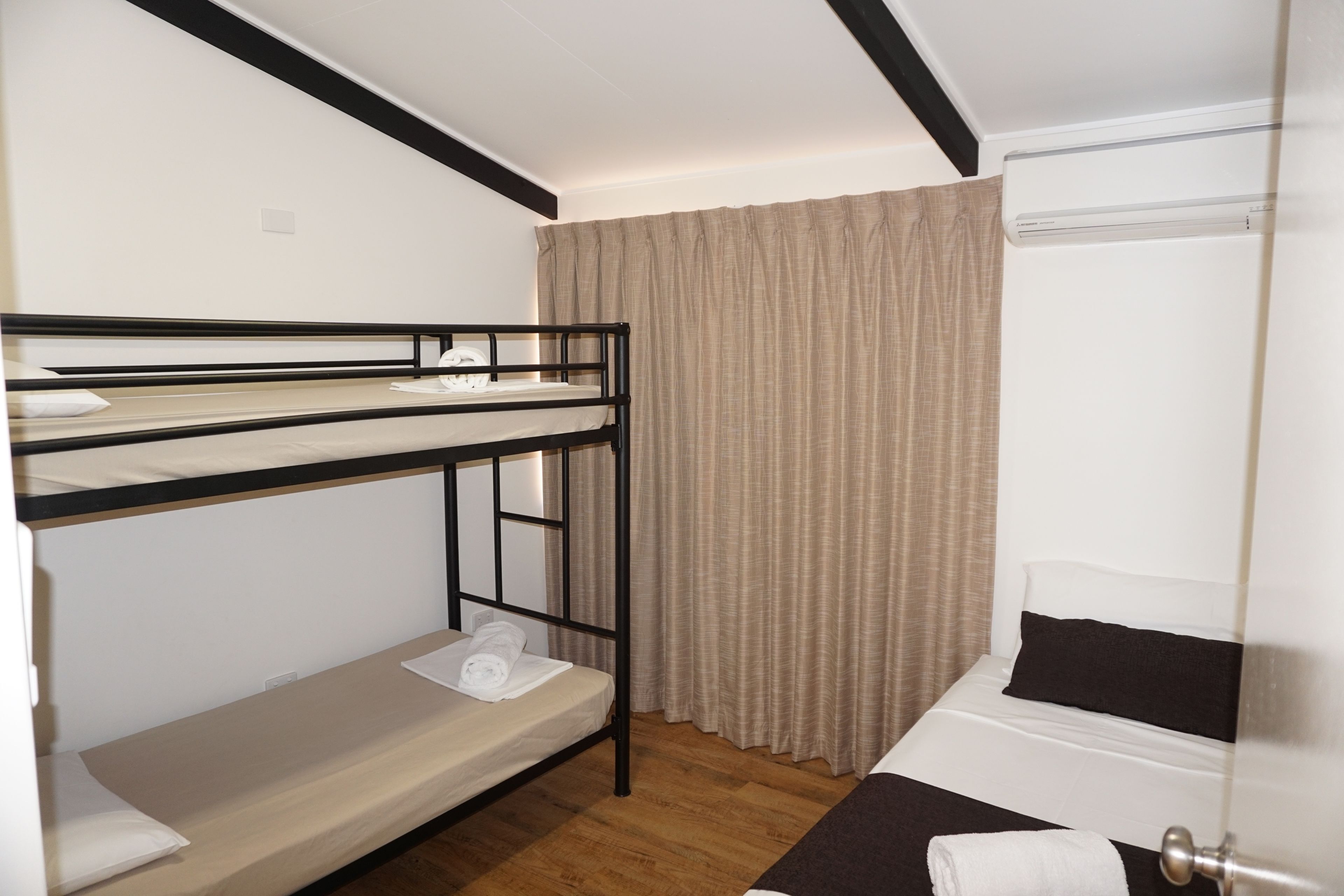 A bunk bed room with a wooden floor, a window with curtains, and a door.