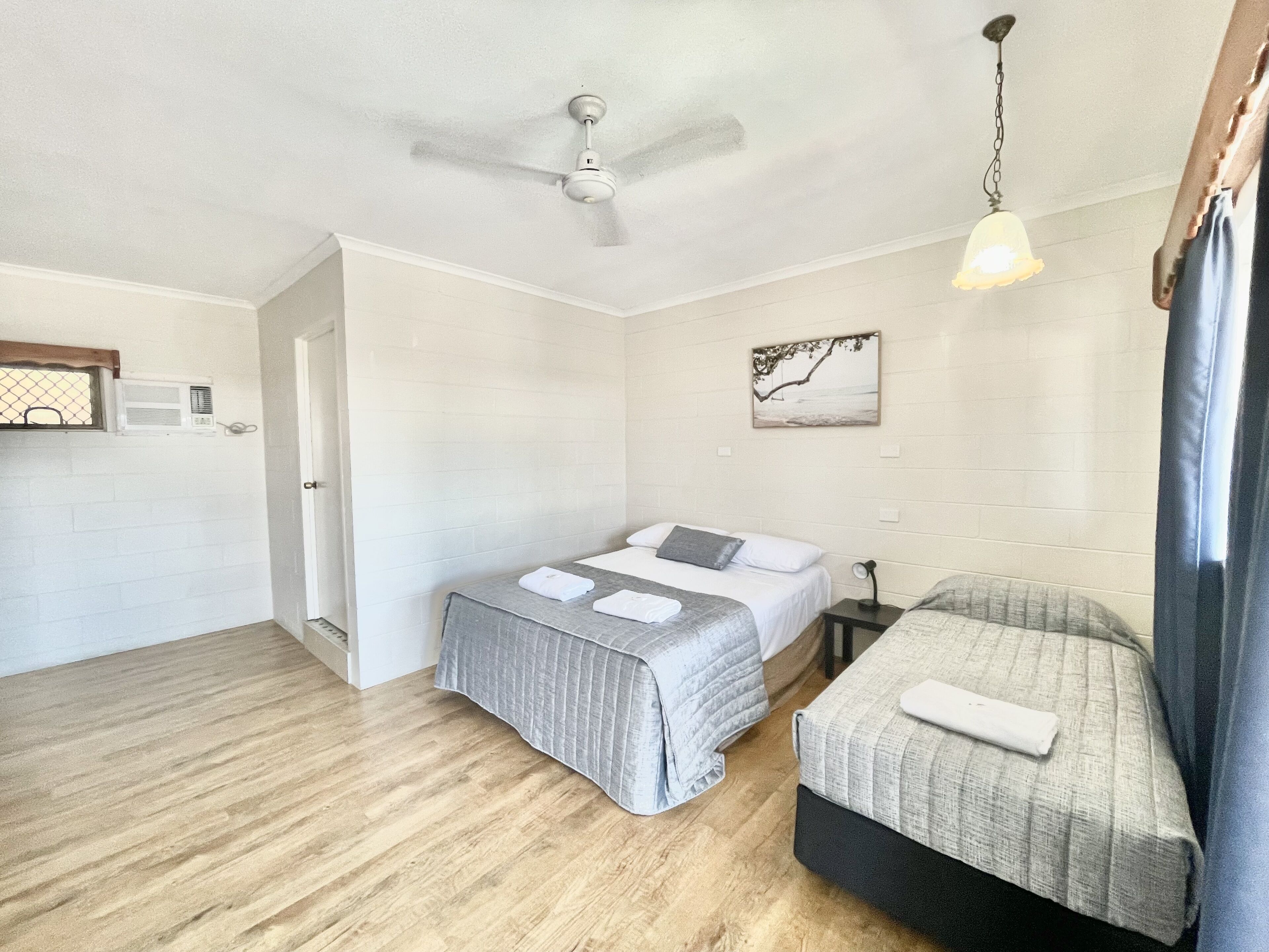 A room with a bed, a smaller bed, a ceiling fan, a wall-mounted air conditioner, and a hanging light fixture.